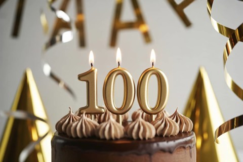 Chocolate 100th birthday cake with flickering candle. Celebration of longevity and reaching a