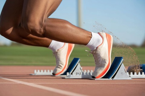 Close-up of athlete in running shoes on starting block at running track. Concept of speed and