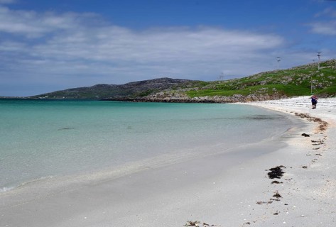 Clear bright blue beach with gentle waves under a cloudless sky, two people at the water's edge,