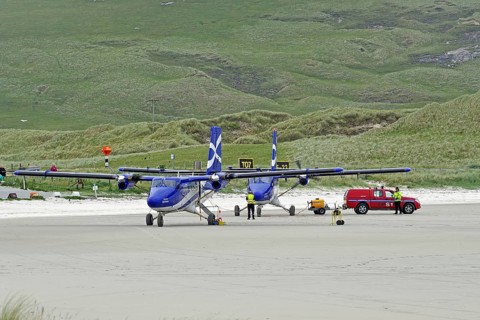 Aeroplanes standing on a runway in front of green hills, accompanied by a red vehicle, Outer