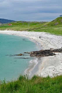Coastal landscape with grassy areas, calm sea and walkers on a white sandy beach, Eriksay, Isle of