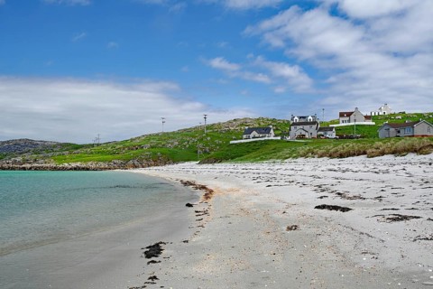 Quiet sandy beach with neighbouring houses under a slightly cloudy sky, Outer Hebrides, Eriksay,
