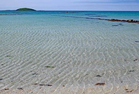 Clear bright blue beach with gentle waves under a cloudless sky, Outer Hebrides, Eriksay, Scotland,