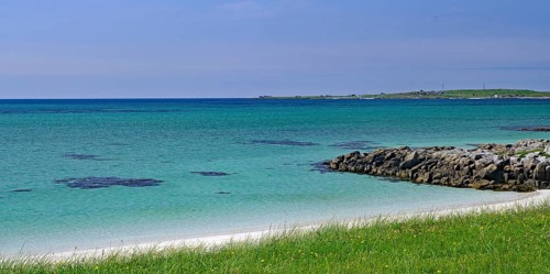 Clear blue sky over a rocky coastline with green grass and blue water, Outer Hebrides, South Uist,