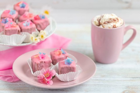 Pink petit fours and a cup of coffee with cream on a table