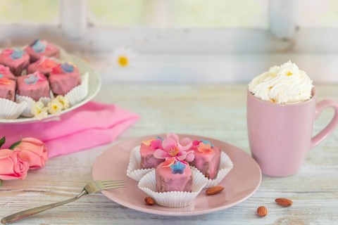 Pink petit fours and a cup of coffee and cream on a table