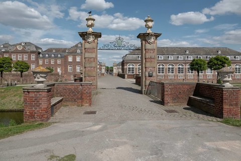 Large brick building with Tor tor and decorated pillars under a blue sky, moated castle