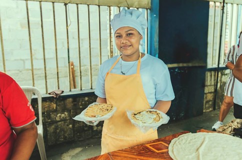 Portrait of a vendor serving and holding two pupusas. Smiling female vendor holding two plates of