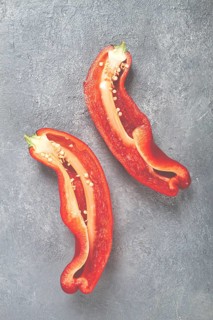Two halves of vibrant red peppers are displayed on a textured gray surface. The seeds and inner