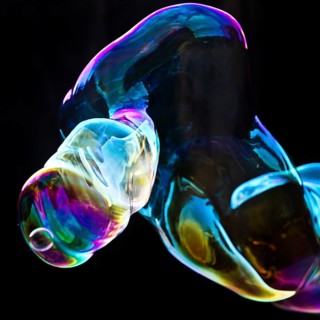 Large, iridescent soap bubble tube in the colours of the rainbow against a black background,
