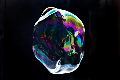 A large iridescent and floating soap bubble in the colours of the rainbow against a black