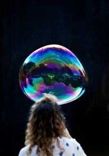 A woman looks at a large iridescent and floating soap bubble in the colours of the rainbow against