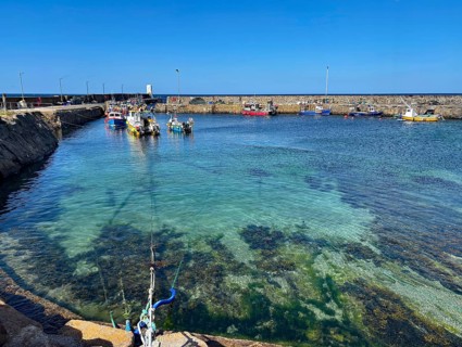 Clear water view of a harbour with small boats surrounded by a stone quay wall, Aberdeenshire,