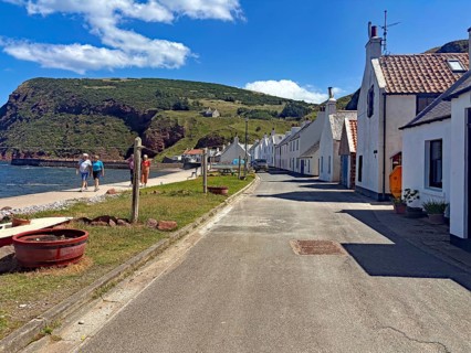 Picturesque coastal road along a small village with houses and a rocky coastline in serene weather,