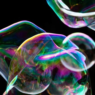 Large, irregular, iridescent soap bubbles in the colours of the rainbow against a black background,