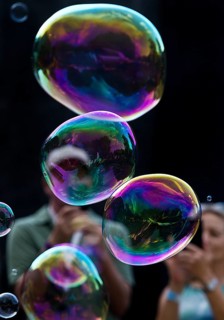 A man and a woman photograph iridescent soap bubbles in front of a black background,