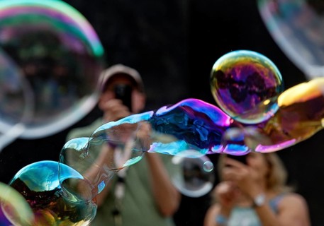 A man and a woman photograph iridescent soap bubbles in front of a black background,