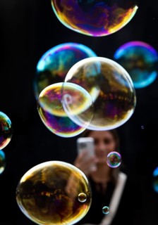 A woman photographs shimmering and floating soap bubbles against a black background,