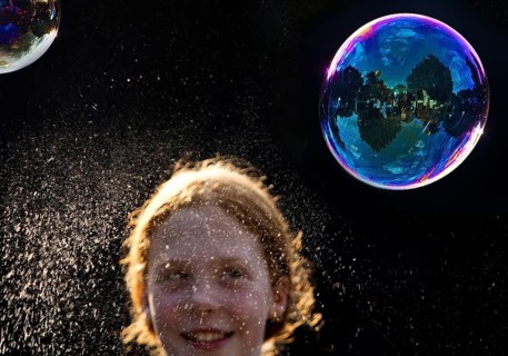 A girl is happy about a shimmering and floating soap bubble in front of a black background,