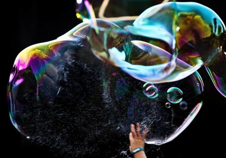 A hand bursts a large iridescent soap bubble against a black background, Recklinghausen, Germany