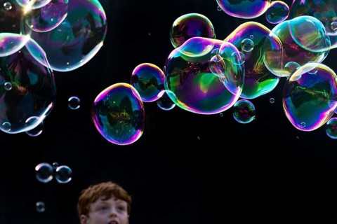 A boy marvels at shimmering and floating soap bubbles against a black background, Recklinghausen,