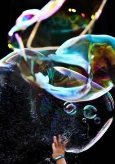 A hand bursts a large iridescent soap bubble against a black background, Recklinghausen, Germany
