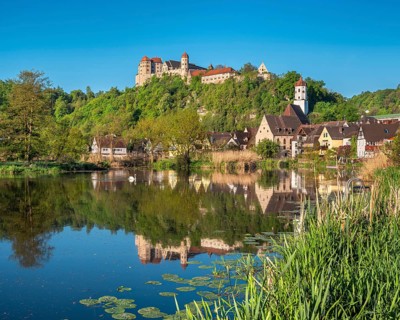 Castle and old town with St Barbara's Church and synagogue reflected in the River Wörnitz, Harburg,