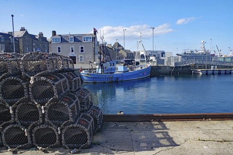 A harbour with fishing boats and stacked nets under a clear sky, Fraserburgh Aberdeenshire,