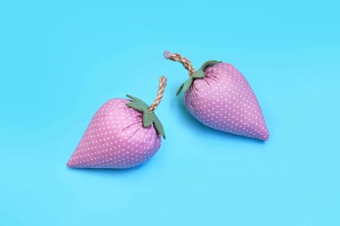 Two handmade pink fabric strawberries on blue background as creative DIY decoration