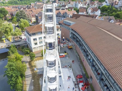 View of a Ferris wheel in a city with surrounding buildings and people in summer, fire brigade