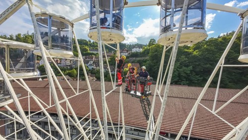 Workers in a Ferris wheel with lifting platform, surrounded by green hills and blue sky, fire