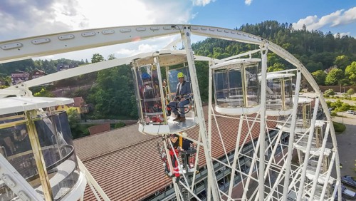 Workers on a platform of a Ferris wheel, surrounded by forest and sky, fire brigade exercise for