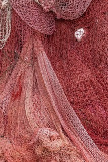 Colourful fishing nets in shades of red that create an interwoven, textured surface, Croatia