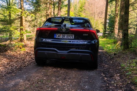 Black car on a forest path surrounded by trees that cast sunlight and shadows, MG 4, Deer E- Car