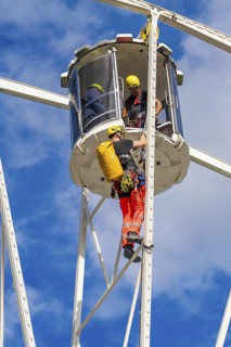 Two workers in safety equipment during maintenance work on a Ferris wheel in a cabin, fire brigade