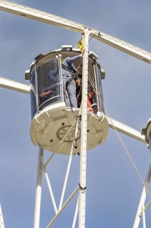 Workers in a cabin of a Ferris wheel carrying out maintenance work, fire brigade exercise for