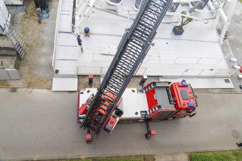 A large fire engine with crane boom is parked on a road, fire brigade exercise for gondola rescue,