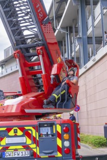 Firefighter resting on an extended lifting platform next to a building, fire brigade exercise for