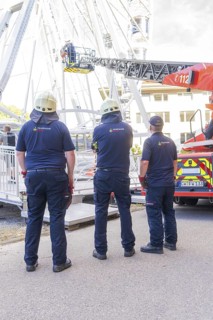 Three firefighters in uniforms standing in front of emergency vehicle with lifting platform, fire