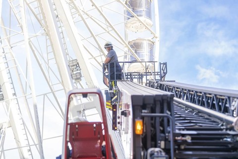 Firefighter on a lifting platform next to a Ferris wheel in front of a clear sky, fire brigade