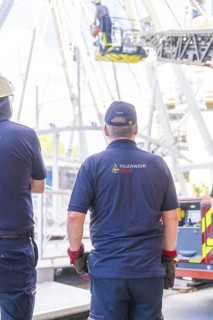 Firefighters stand ready in uniform while a rescue operation takes place on the Ferris wheel, Fire