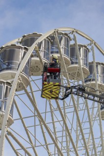 Fireman in the rescue cage is lifted to the cabins of the Ferris wheel, blue sky as background,