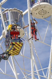 Rescue workers on a Ferris wheel during safety work under blue sky, fire brigade exercise for