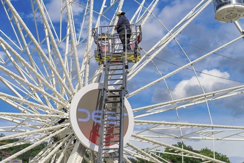A worker on a ladder, the Ferris wheel and the blue sky characterise the scene, Fire brigade