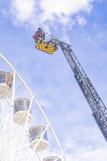 Zoom on fire brigade ladder close to the Ferris wheel in front of blue sky, fire brigade exercise