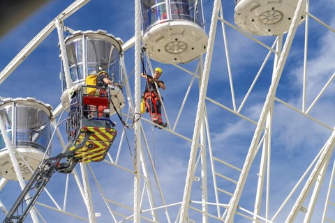 Workers secured on a Ferris wheel during rescue work under blue sky, fire brigade exercise for