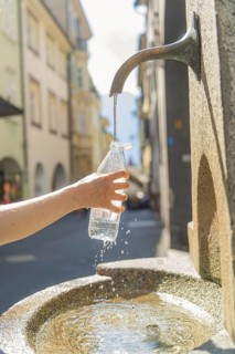 Close-up of a hand filling a bottle at a flowing fountain, Merano, South Tyrol, Italy