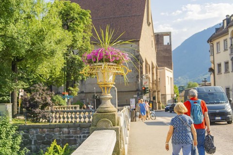 A couple walks across the stone bridge, view of mountains and flowers, Merano, South Tyrol, Italy
