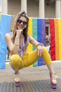 Young woman crouching and smiling brightly, wearing stylish sunglasses and vibrant, colorful