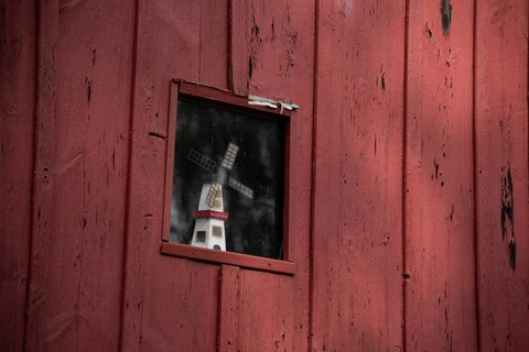 A small window in a red wooden faÃ§ade with a windmill as decoration behind it, Prerow,